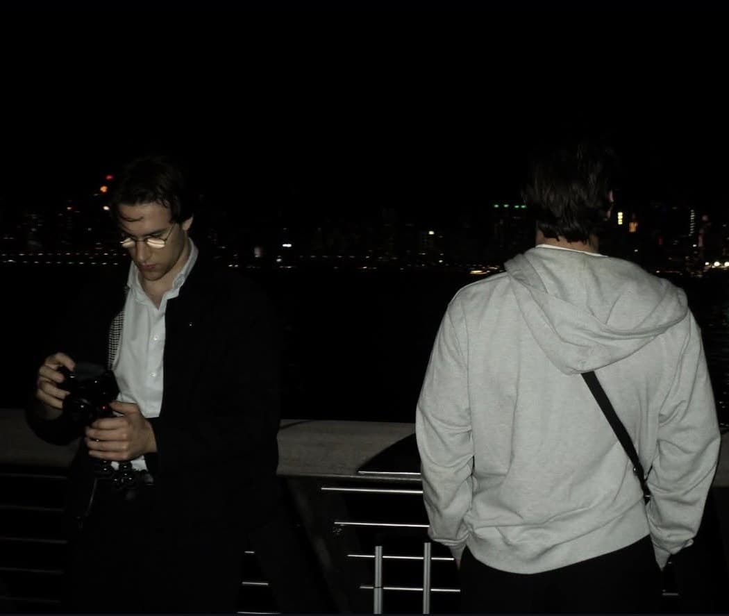 Twee mensen bij de reling langs het water, met de skyline van Hongkong bij nacht.